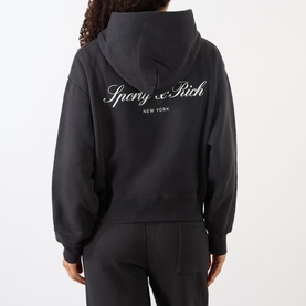 Model wearing Sporty and Rich Signature Logo Hoodie in Faded Black, back view showing contrast script logo, styled with matching sweatpants.