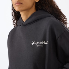 Model wearing Sporty and Rich Signature Logo Hoodie in Faded Black with white chest logo, close-up crop showing hood detail