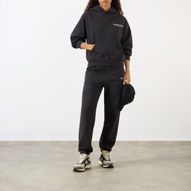 Model wearing Sporty and Rich Signature Logo Hoodie in Faded Black with matching joggers, styled with a cap and chunky trainers.