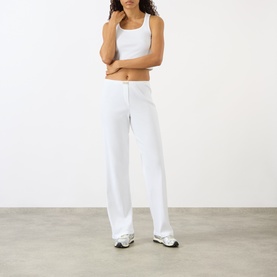 Model wearing Sporty and Rich Signature Logo Ring Lounge Pants in white, with elasticated waist and wide-leg fit, styled with a white crop top.