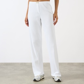 Model wearing Sporty and Rich Signature Logo Ring Lounge Pants in white, with elasticated waist and side pockets, styled with white trainers.