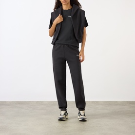 Model wearing Sporty and Rich Signature NY Logo Sweatpants in Faded Black with matching vest and graphic tee, styled with chunky trainers.
