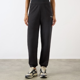 Model wearing Sporty and Rich Signature NY Logo Sweatpants in Faded Black with elasticated cuffs and waist, styled with white trainers.