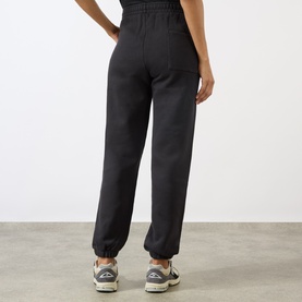 Model wearing Sporty and Rich Signature NY Logo Sweatpants in Faded Black, elasticated cuffs and waist, styled with trainers, rear view.