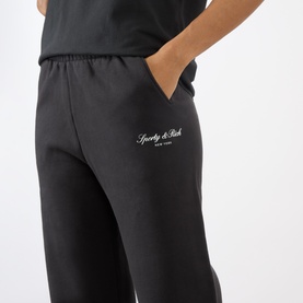 Model wearing Sporty and Rich Signature NY Logo Sweatpants in Faded Black, with elasticated waist, side pockets and embroidered logo detail.