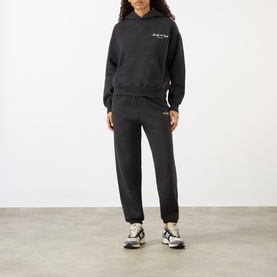 Model wearing Sporty and Rich Signature NY Logo Sweatpants in Faded Black with matching hoodie and multicolour trainers.