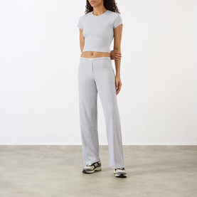 Model wearing Sporty and Rich Signature Logo Rib Sweatpants in grey, straight leg, ribbed texture, styled with a grey crop tee and trainers.