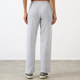 Model wearing Sporty and Rich Signature Logo Rib Sweatpants in grey, straight-leg cut with elasticated waist, styled with grey trainers.