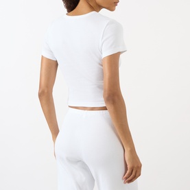 Model wearing Sporty and Rich Signature Logo Rib Baby T-Shirt in white, showing ribbed texture, round neck and cropped hem. Styled with white