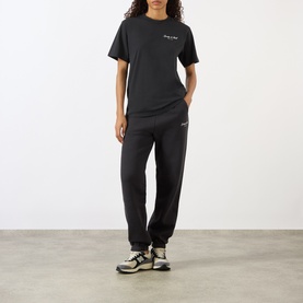 Model wearing Sporty and Rich Signature NY Logo T-Shirt in Faded Black, styled with matching black joggers and chunky trainers.