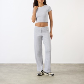 Model wearing Sporty and Rich Signature Logo Rib Baby T-Shirt in Heather Grey with matching wide-leg trousers and chunky trainers.