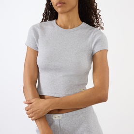 Model wearing Sporty and Rich Signature Logo Rib Baby T-Shirt in Heather Grey, ribbed texture, round neck, short sleeves, styled with matching shorts.