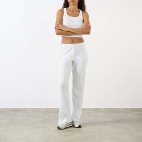Model wearing Sporty and Rich Signature Logo Tank Top in white with white wide-leg trousers and chunky trainers
