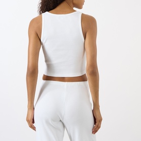 Model wearing Sporty and Rich Signature Logo Tank Top in white, back view, styled with matching white wide-leg trousers.