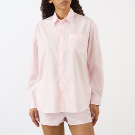 Model wearing Sporty and Rich Signature Logo Shirt in Clear Pink, relaxed fit with chest pocket and logo detail, styled with matching shorts.