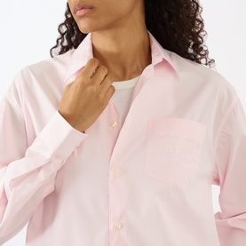 Model wearing Sporty and Rich Signature Logo Shirt in Clear Pink, relaxed fit cotton with pointed collar, chest pocket and button fastenings.