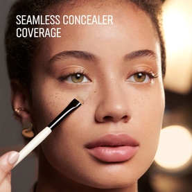 Model with Bobbi Brown brush applying concealer under eye, close-up beauty shot showing seamless coverage technique