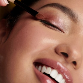 Bobbi Brown brush set applied to eyelid, creating a rosy shimmer eye look on smiling model with glossy lips