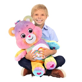 Boy hugging large Care Bears rainbow-coloured plush bear toy, multicoloured with heart emblem on tummy, roughly 60cm tall
