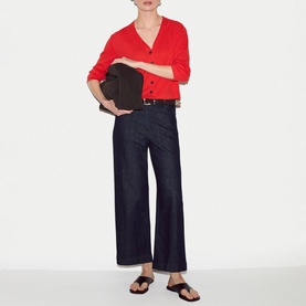 Model wearing Jigsaw red V-neck cardigan with dark wide-leg jeans, black sandals, carrying a dark brown clutch bag.