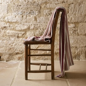 Christys bath towel in multi stripe draped over a rustic wooden chair against a stone wall backdrop
