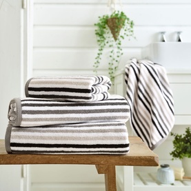 Deyongs Linear Stripe Towel Chrome in grey and white stripes, stacked on wooden bench in bathroom setting, with hand towel on rail