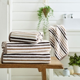 Deyongs Linear Stripe Towel Natural in cream and brown stripes, stacked in three sizes on a wooden bench in a bathroom setting