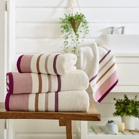 Deyongs Portland Stripe Towel in Jewells, stacked folded cotton towels with purple, pink and tan stripe border detail on wooden bench.