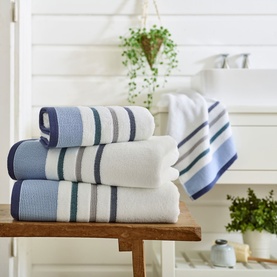 Deyongs Portland Stripe Towel Oceanic in white with blue, grey and teal stripes, shown folded in a stack of four in a bathroom setting.