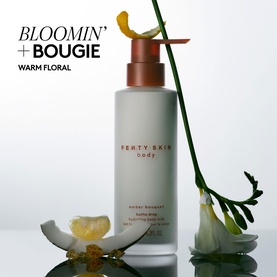 Fenty Skin Amber Bouquet Butta Drop Hydrating Body Milk in frosted grey pump bottle with rose gold cap, styled with white florals and green stems