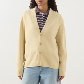 Model wearing Guest In Residence butter cashmere cardigan with V-neck and button front, styled with striped polo shirt and blue jeans.