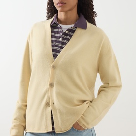 Model wearing Guest In Residence butter cashmere cardigan with three buttons, styled over a striped shirt with purple collar.