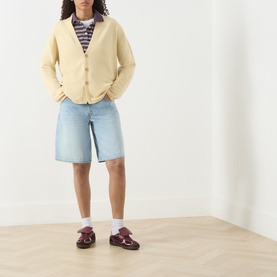 Model wearing Guest In Residence butter cashmere cardigan with denim shorts, striped top, white socks and burgundy Mary Jane shoes