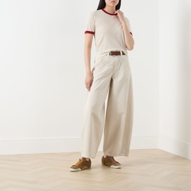 Model wearing Guest In Residence Airy Ringer T-Shirt in cream with contrast red trims, styled with wide-leg trousers and tan trainers.