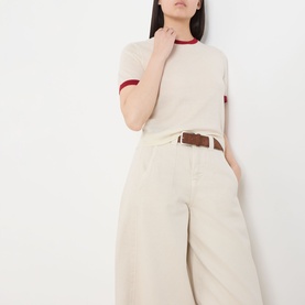 Model wearing Guest In Residence Airy Ringer T-Shirt in cream with red contrast trims, styled with wide-leg cream trousers and brown belt.