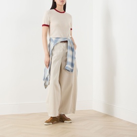 Model wearing Guest In Residence Airy Ringer T-Shirt in cream with contrast burgundy trims, styled with wide-leg trousers and plaid shirt tied at