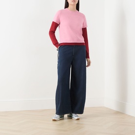 Model wearing Guest In Residence Double Layer Top in pink with burgundy double-layer sleeves, styled with wide-leg dark denim jeans and grey trainers.