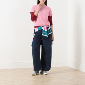 Model wearing Guest In Residence Double Layer Top in pink with burgundy double-layer sleeves, styled with navy wide-leg trousers and a striped shirt