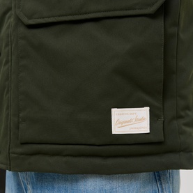 Model wearing Jack & Jones Norrebro Padded Barn Jacket in Rosin, close-up of patch pocket and branded woven label, styled with blue jeans