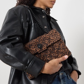 Model carrying Kurt Geiger Kensington Leopard Crossbody Bag in brown leopard-print suede with black chain strap and eagle hardware