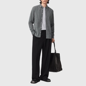 Model wearing All Saints light grey long-sleeve shirt with black wide-leg trousers, carrying black tote bag, styled with black loafers.