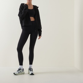 Model wearing Lululemon Energy Longline Sports Bra in black, styled with black zip hoodie, black leggings and grey chunky trainers.