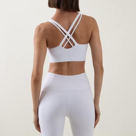 Model wearing Lululemon Energy Longline Bra in white, cross-back strap detail, styled with matching white high-waist leggings.