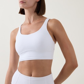 Model wearing Lululemon Energy Longline Bra in white, with scoop neckline and wide straps, styled with white leggings.