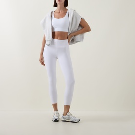Model wearing Lululemon Energy Longline Bra in white, styled with matching white high-waist leggings, draped grey jacket and white trainers.