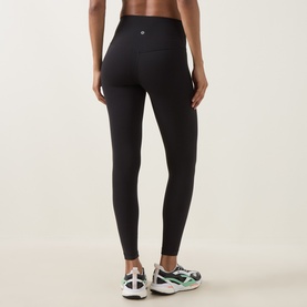 Model wearing Lululemon black high-waist leggings, rear view, styled with green and white trainers