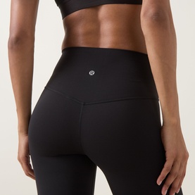 Model wearing Lululemon black high-waist leggings, rear view showing logo detail, styled with a black sports bra