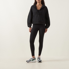 Model wearing Lululemon black leggings, styled with a black half-zip pullover and white and green chunky trainers.
