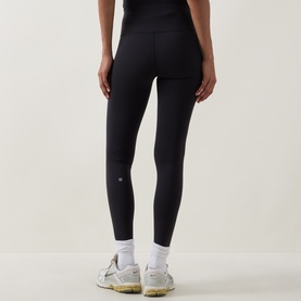 Model wearing Lululemon black leggings, rear view, styled with white trainers.