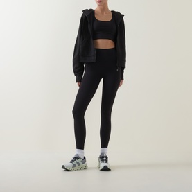 Model wearing Lululemon Scuba Oversized Full-Zip Hoodie in black, styled with black sports bra, leggings and grey trainers.